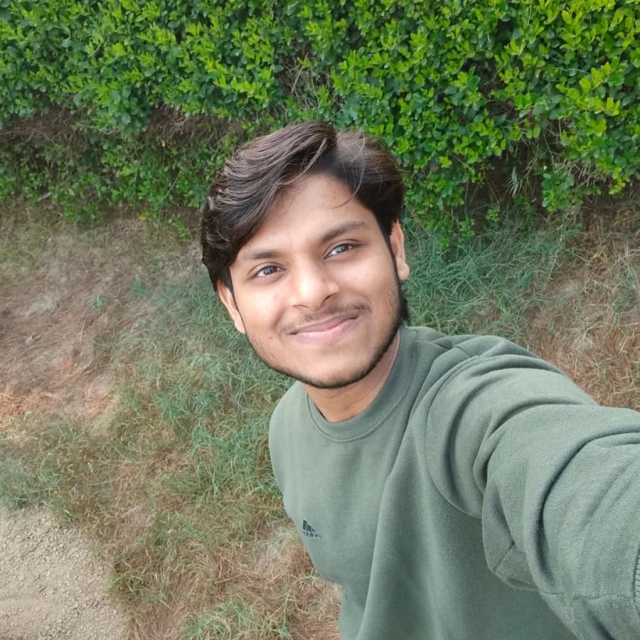 Selfie of Chandan in a green sweatshirt with a green hedge behind him.